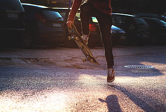 Skateboarder performing trick on asphalt street at sunset