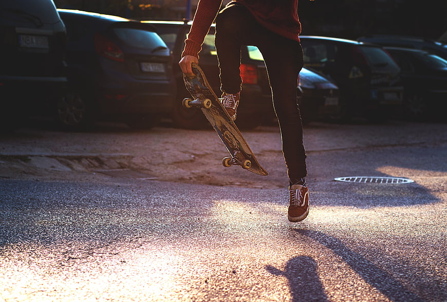 Skateboarder performing trick on asphalt street at sunset