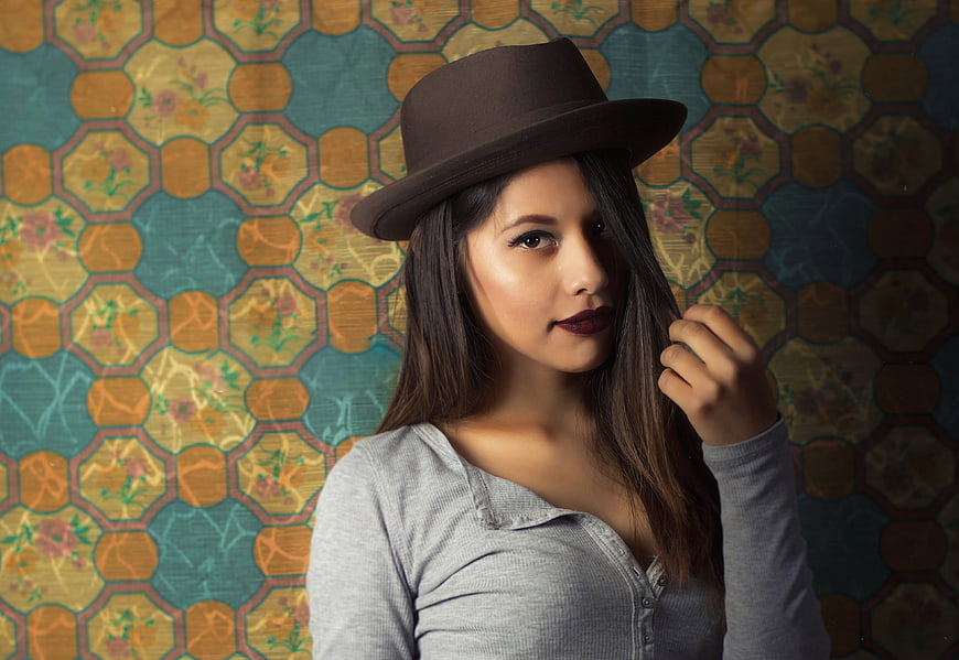 Stylish woman in brown hat against vintage patterned background
