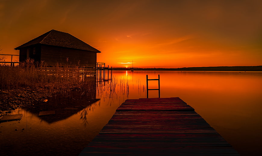 Serene Sunset Over Lake With Wooden Dock And Cabin