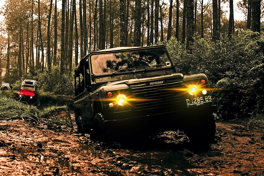 Off-road Land Rover Defender driving on muddy forest trail