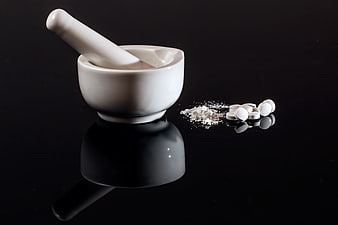White mortar and pestle with crushed pills on black background