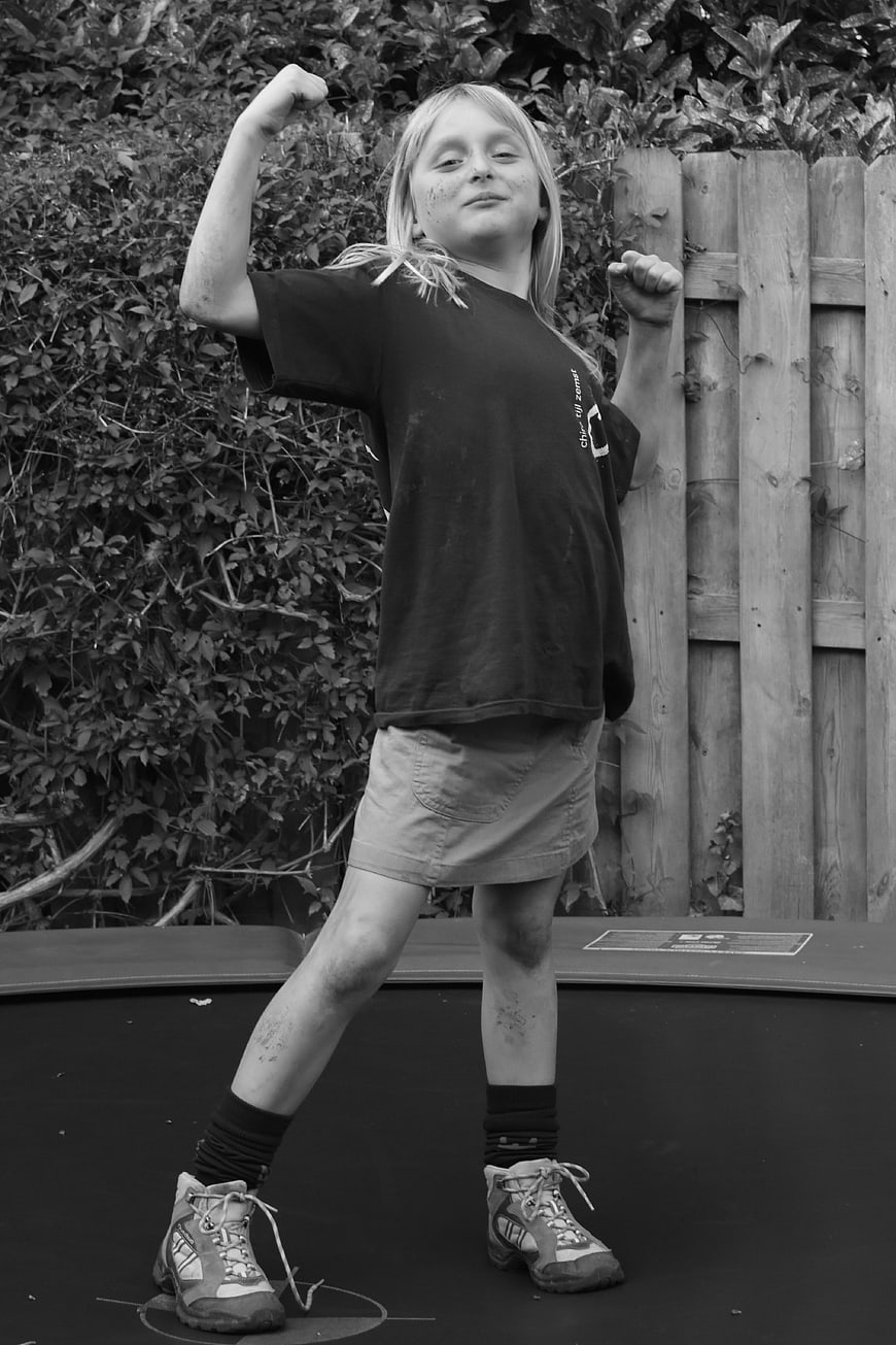 Confident young girl flexing arms on trampoline in black and white