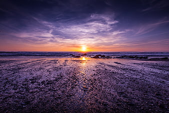 Vibrant Purple Sunset Over Rocky Beach With Ocean Reflection
