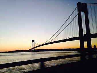 Silhouette of suspension bridge over water at sunset
