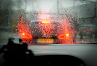 Rainy car dashboard view with blurred red taillights