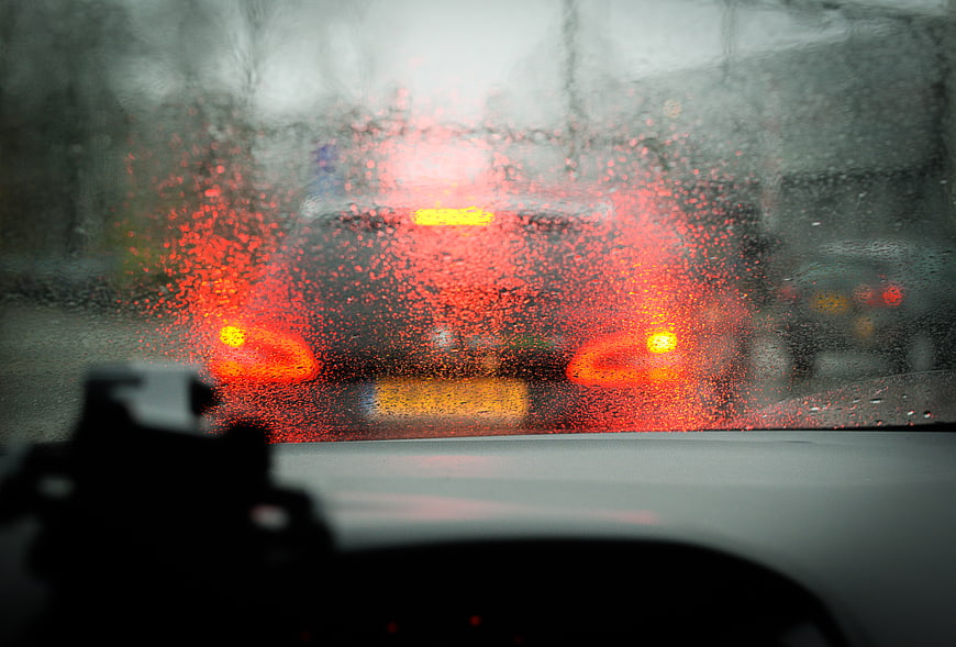 Rainy car dashboard view with blurred red taillights