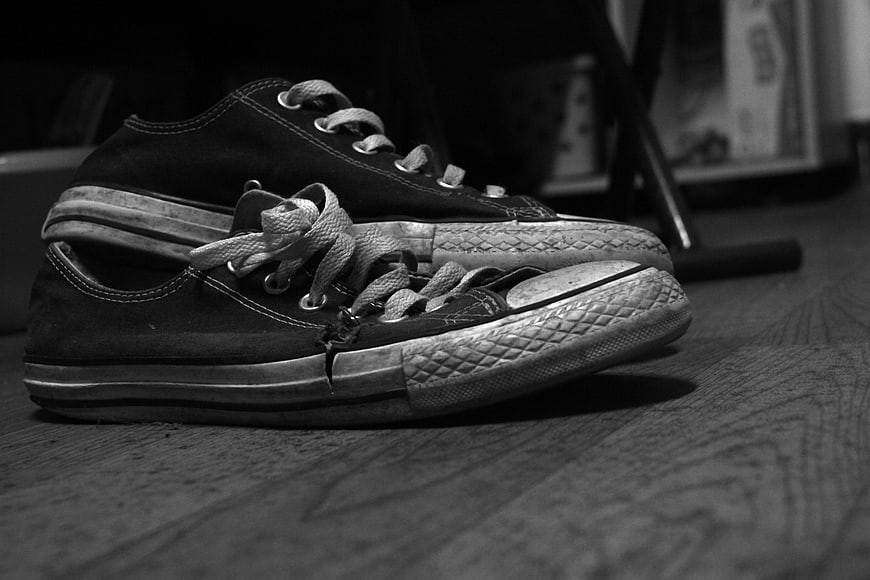 Vintage black and white worn canvas sneakers on wooden floor