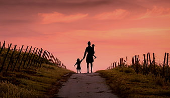 Silhouette of Mother Walking with Two Children on Country Road at Sunset