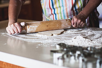Hands Rolling Dough With Wooden Pin On Floured Kitchen Counter