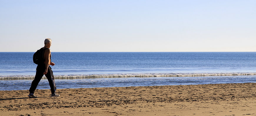 Senior man walking on sandy beach with backpack