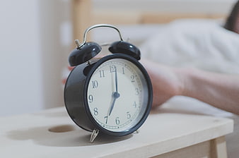 Black alarm clock on bedside table with person waking up in background