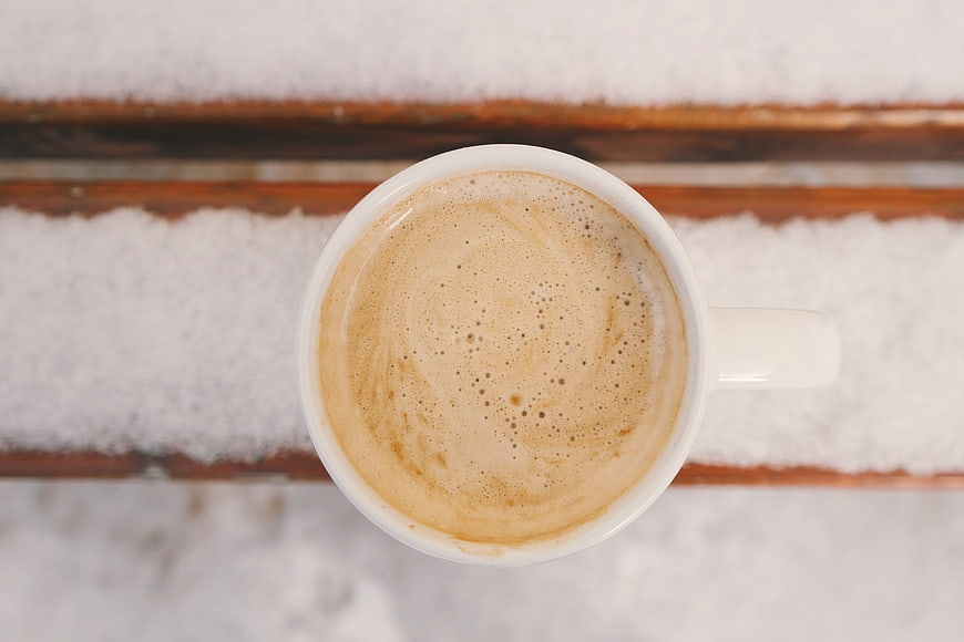 Top View of Hot Coffee in White Mug on Snowy Wooden Bench