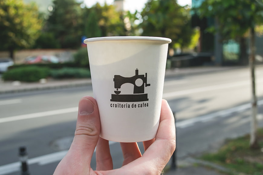 Hand holding white coffee cup with sewing machine logo on street