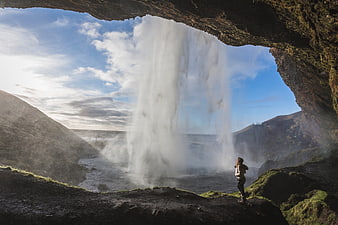Woman standing behind a massive waterfall inside a cave