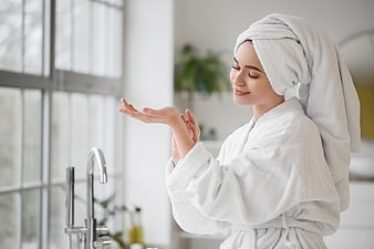 Woman in white robe applying skincare lotion in bathroom