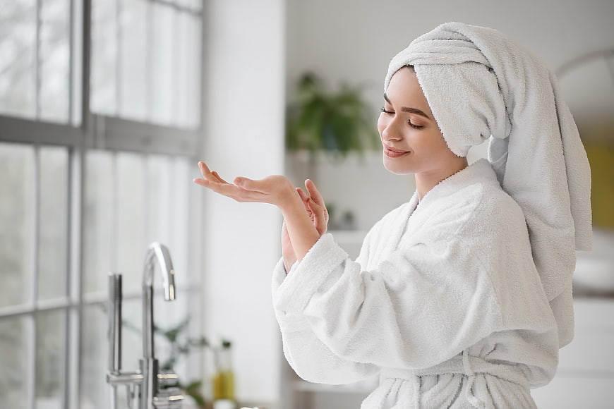 Woman in white robe applying skincare lotion in bathroom