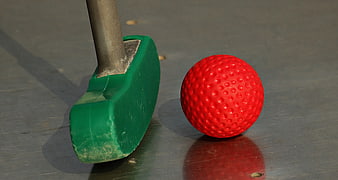 Close-up of green mini golf putter and red ball on gray surface