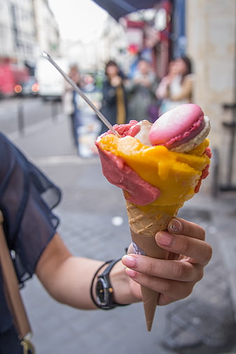 Hand holding colorful gelato cone with macaron on city street