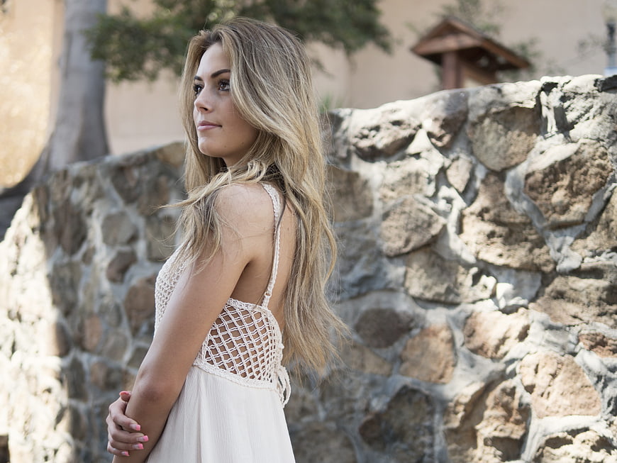 Young woman in white crochet dress standing against rustic stone wall