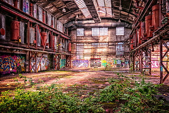 Abandoned industrial factory interior with graffiti and overgrown weeds