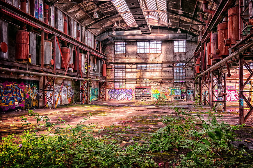 Abandoned industrial factory interior with graffiti and overgrown weeds