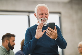 Happy Senior Man Video Calling on Smartphone in Office