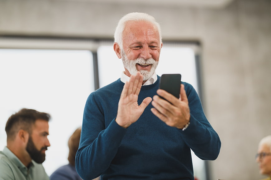 Happy Senior Man Video Calling on Smartphone in Office