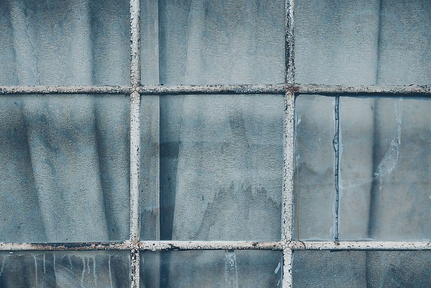 Textured gray window with peeling white grid and translucent curtain