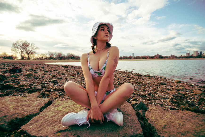 Young woman in floral bikini and bucket hat sitting on rocky shoreline