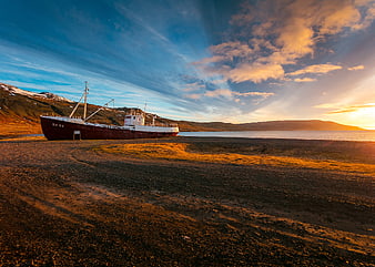 Abandoned ship on rocky beach at sunset with dramatic sky