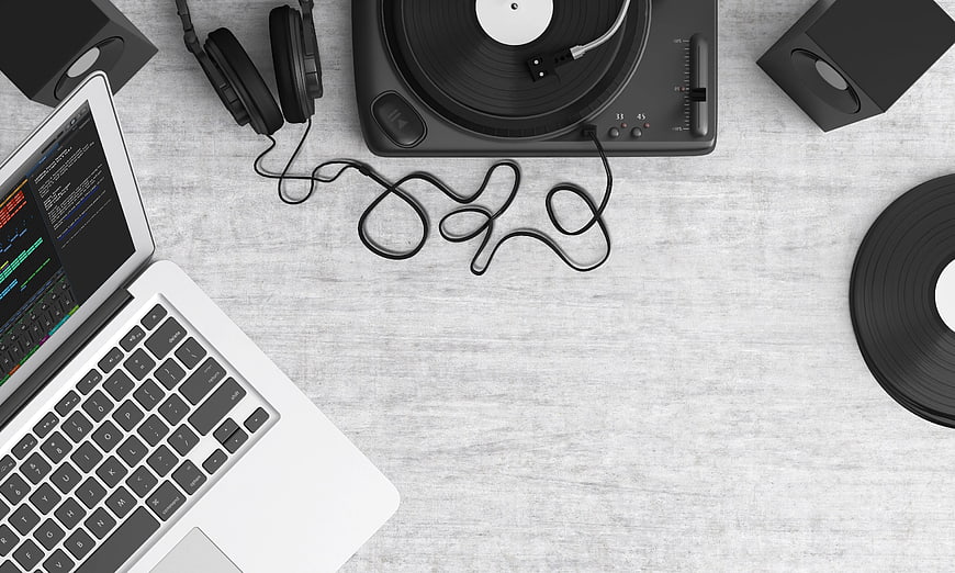 Top view of laptop, turntable, and headphones on gray desk