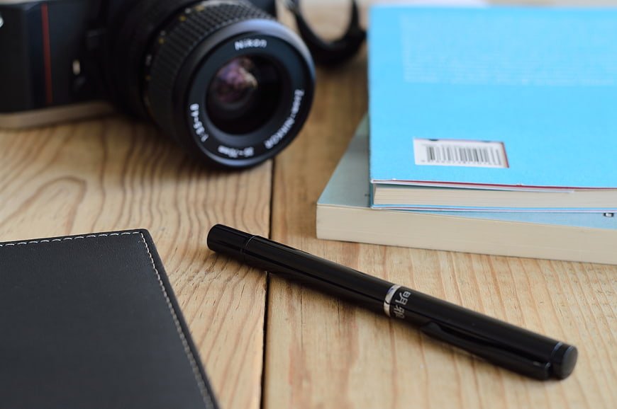 Camera, books, and pen on wooden desk workspace