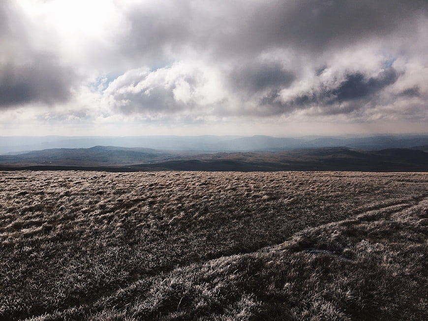 Frosty moorland landscape with dramatic cloudy sky and distant mountains