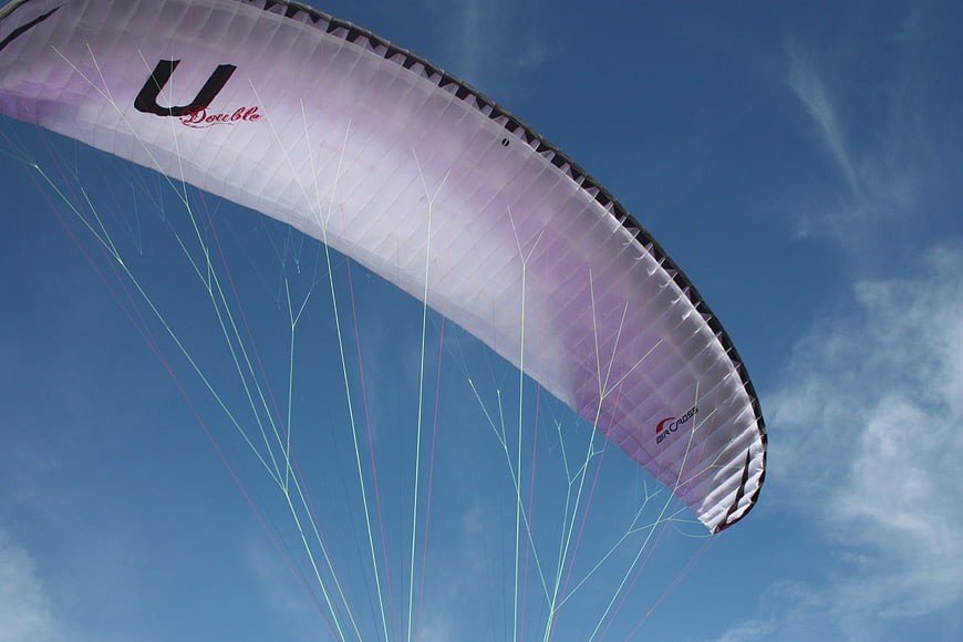 White and purple paraglider wing against blue sky
