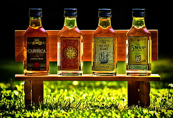 Four Rum Bottles On Wooden Bench In Sunlit Grass
