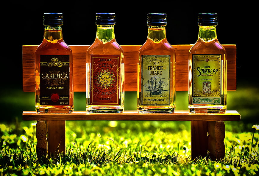 Four Rum Bottles On Wooden Bench In Sunlit Grass
