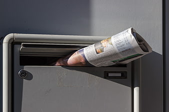 Rolled newspaper sticking out of gray metal mailbox