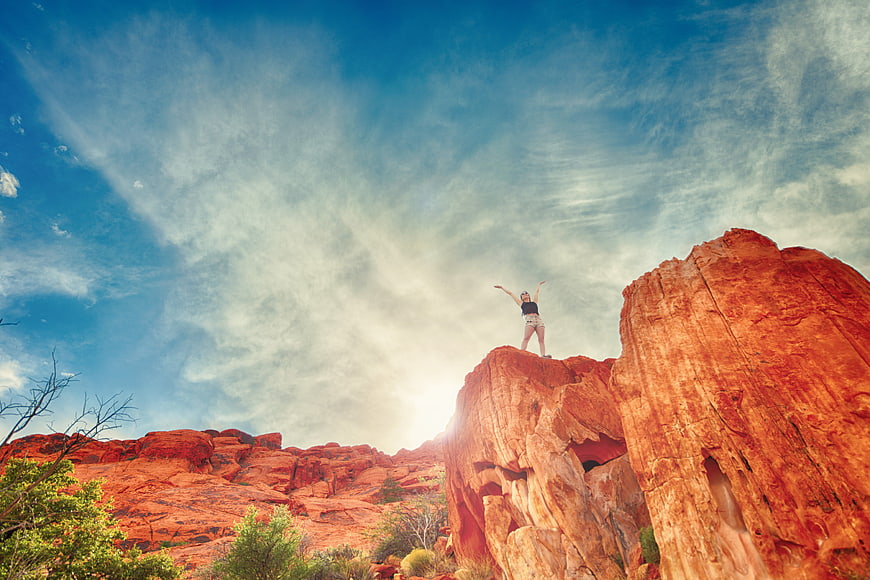 Woman standing on red rock formation with arms raised in desert landscape