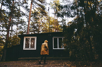 Person in yellow raincoat walking past dark cabin in forest