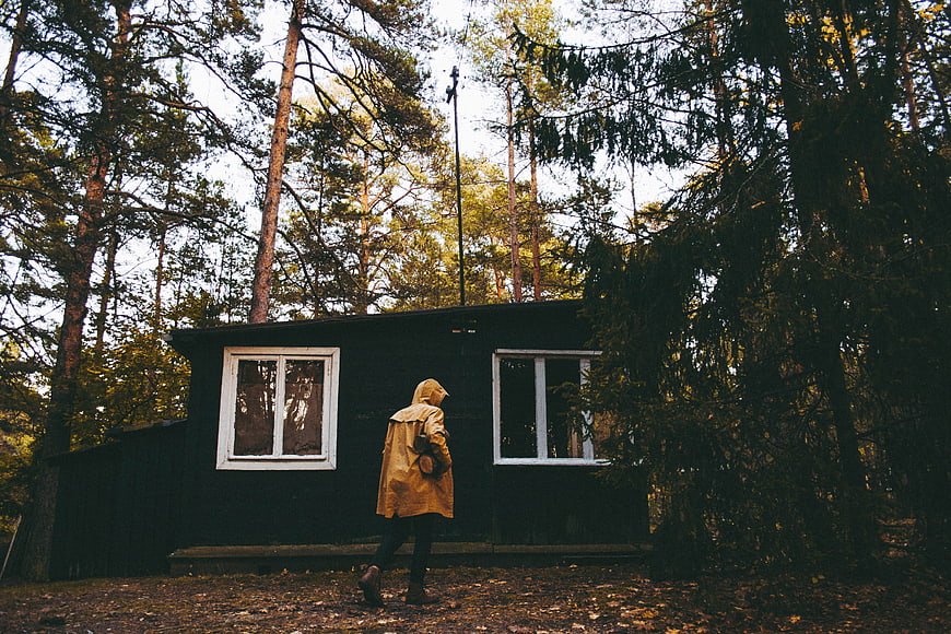 Person in yellow raincoat walking past dark cabin in forest