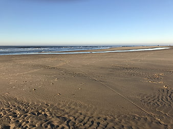 Wide sandy beach with ocean waves and clear blue sky