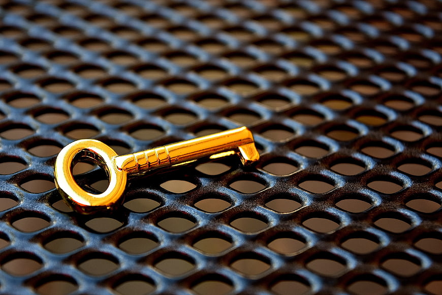 Golden Key on Dark Perforated Metal Grid Background
