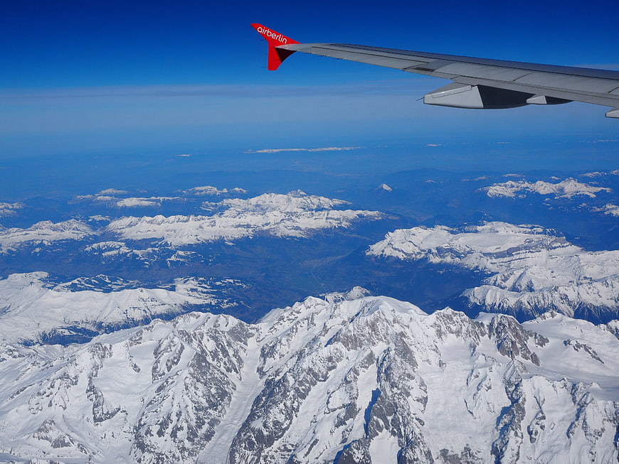 Airplane wing view over snow-capped Alps mountains