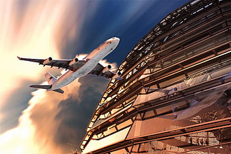 Airplane taking off near modern glass architecture at sunset