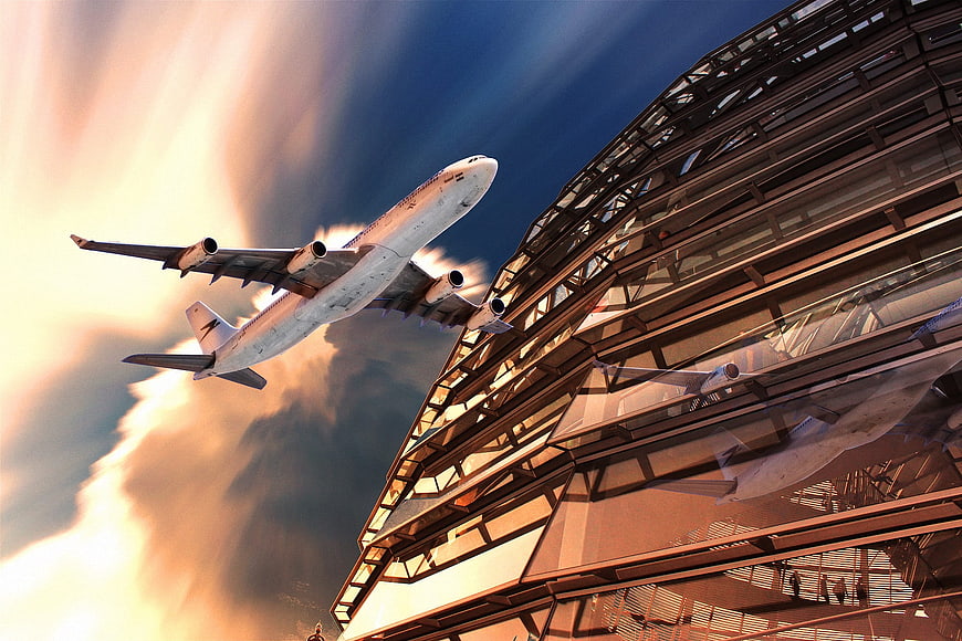 Airplane taking off near modern glass architecture at sunset
