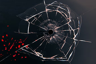 Shattered glass with bullet hole and red splatter on dark background