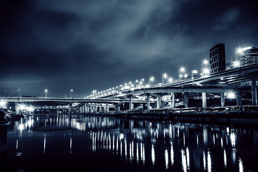 Nighttime cityscape with illuminated highway bridge and river reflections