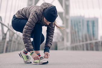 Woman tying running shoes on urban bridge