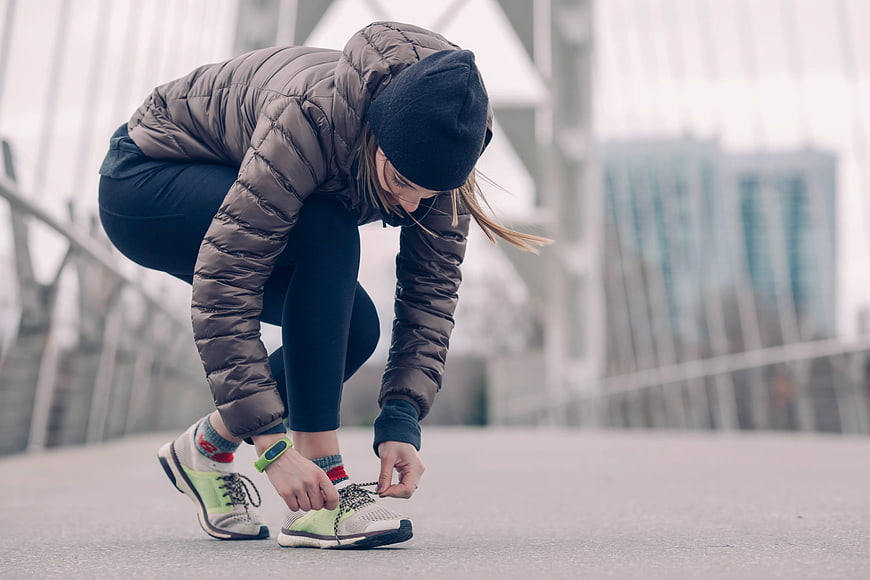 Woman tying running shoes on urban bridge